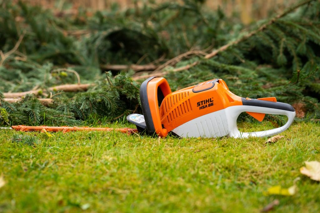 Electric hedge trimming tool laying next to various branches of a a larger hedge.